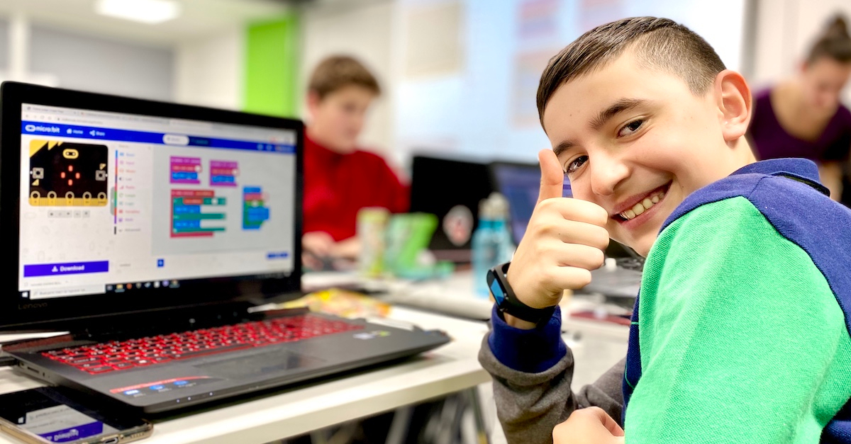 boy sitting at computer looks over shoulder smiling signaling thumbs up