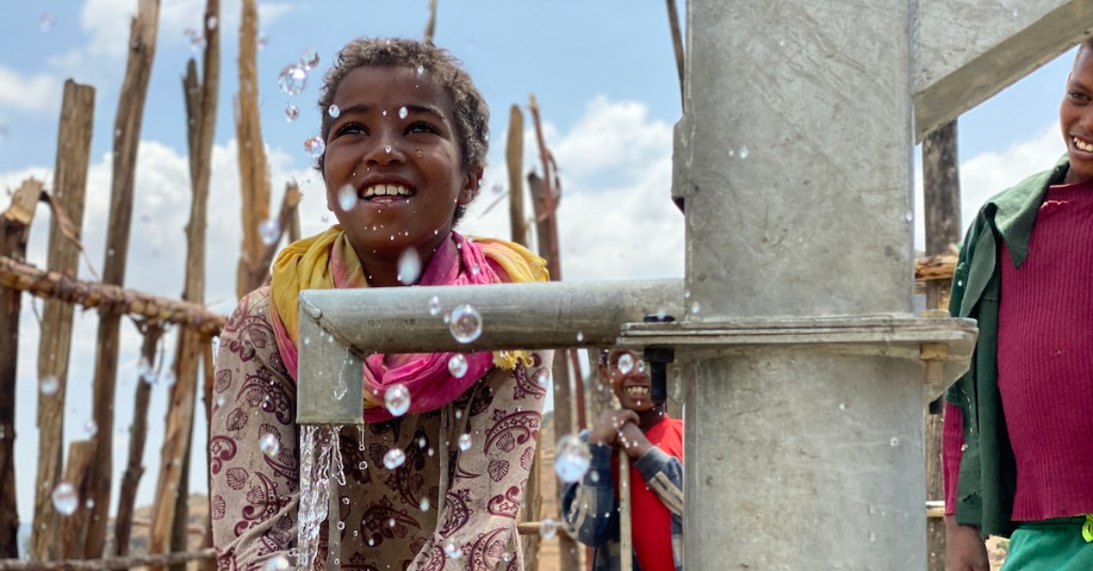 girl holds her hands under an outdoor well pump inspiring nonprofit photos of 2023
